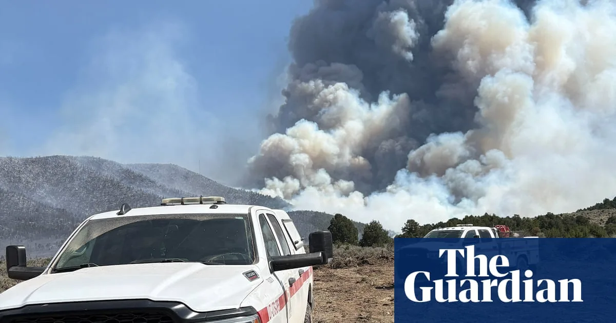Firefighters work near a wildfire burning in dry terrain as smoke rises over the Utah landscape